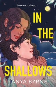 Illustrated cover for In the Shallows. Two teenage girls lounge on the beach together on a partially cloudy night. One girl has medium, brown skin and shoulder-ish wavy brown hair and maybe a purple t-shirt. She's leaning forward, just barely on the cover, with her head resting atop the other girl's head. The other girl is leaning back against her shoulder. She has a lighter complexion and looks as if she could be of Asian descent. She has similar color hair, but hers is in a bob, and she's wearing what might be a white sleeveless shirt. The moon shines brightly overhead. 