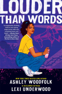 A young black woman is squatting down near a dark blue wall. There is a hot pink megaphone painted on the wall and she is holding a spray paint can.