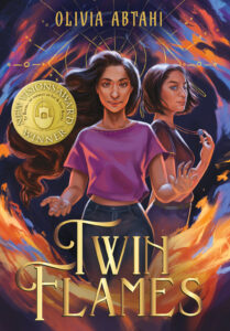 Illustrated cover of Twin Flames. Twin teenage girls are wreathed in flame, with a gold stylized eye behind them. The twin facing the viewer has waist-length brown hair and has her hands out, like she might be conjuring the fire. She is wearing a pink shirt and blue jeans. The twin turned to the right is looking over her shoulder and is holding a blue circle pendant necklace. She has chin-length brown hair and is wearing a gray shirt and lighter blue jeans. They both look serious, but they have an air of watching and waiting.