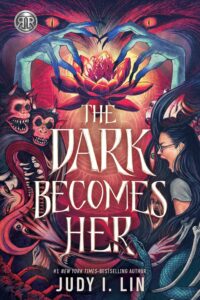The Dark Becomes Her book cover. There are eyes with fur around them at the top of the image and long spiky nailed skinny hands are curling above a lotus. On the left side there are faces that seem like monkeys with sharp teeth and horns. On the right side is a young dark haired woman wearing glasses who is screaming or yealling. There is also a snake in the bottom corner. There are eyes and faces within hair and other winding things. 