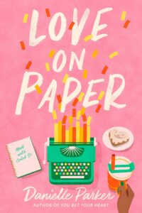 Pink background on this cover with a green typewriter toward the bottom. Instead of a sheet of paper in the typewriter, multiple strips of paper of various shades of orange yellow and red are in there and look almost like candles. There are bits of the same paper up in the air like confetti. To the left is a notebook open to a page that says meet with Caleb. On the right is a brown skinned hand with green nail polish holding a travel mug. There is also a plate with a heart shaped frosted baked good. 