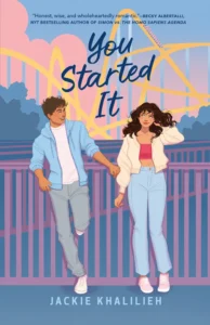 A young man and young woman are standing outside leaning on a fence or bridge with slats. They are smiling at each other. The sky is pink and blue and there are trees in the background. 