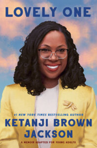 Book cover for Lovely One has. smiling Black woman with shoulder length dark curly hair. She's wearing glasses, is smiling and is wearing a white blouse and yellow blazer. There is a blue sky with puffy pink clouds behind her. 