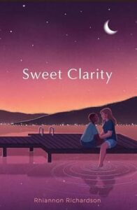 Book cover of Sweet Clarity by Rhiannon Richardson. The setting is a lake with two hills overlapping in the background. It is evening with some stars and a crescent moon with a sweet orange and purple sunset. The lake has a dock with two people sitting on it. One person is slightly smaller with dark skin and short cropped dark hair. The other person has lighter skin and light brown shoulder length hair and has one foot hanging down into the water. The two people are facing each other and may be holding hands between them. They seem to be about to kiss. 