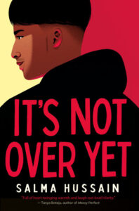 Illustrated cover of It’s Not Over Yet by Salma Hussain. A teenage boy has his back to the viewer, though his face is in profile. He has medium brown skin and short black hair, and he is wearing a black hoodie. His face is illuminated by a beam of light (maybe sunlight?), and his left ear is illuminated by a red light. He has a thoughtful expression on his face.